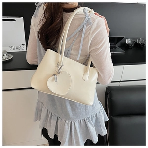 Chic cream leather tote bag with heart charm shown on model in a modern office setting