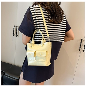 Detail of a light beige crocodile pattern handbag with front flap pockets and knot handle