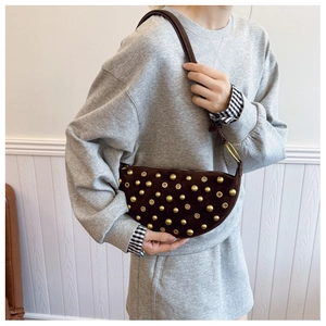Detail of a brown suede half-moon shoulder bag with golden rivets and a biker style
