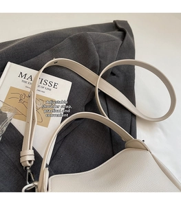 Détail de la bandoulière réglable sur un sac seau en cuir crème avec boucles argentées