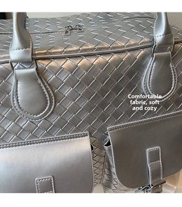 Detail of silver woven travel bag showing Intrecciato texture and metal zipper pockets