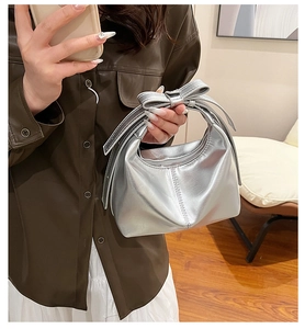 Silver metallic dumpling bag with a bow handle detail shown in a casual lifestyle setting