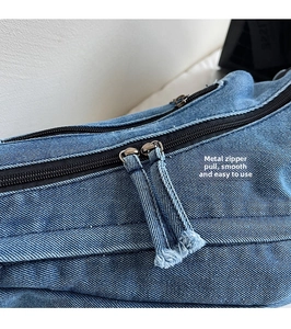Close-up of blue denim crossbody bag with smooth dual zippers and fabric pulls