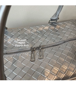 Close-up of dual gunmetal zippers on silver woven texture travel bag detail