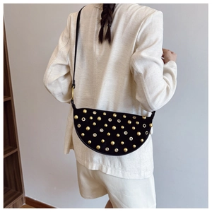 Detail of a crescent-shaped suede shoulder bag featuring gold rivets on a black finish