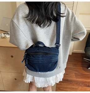 Detail of blue denim crossbody bag featuring a curved messenger shape and wide shoulder strap