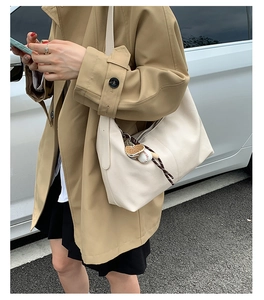 Détail du sac hobo blanc cassé avec breloque baseball sur une tenue de trench-coat