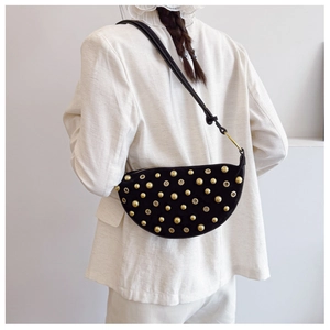 Detail of black suede crescent bag with gold rivet studs worn on a white blazer