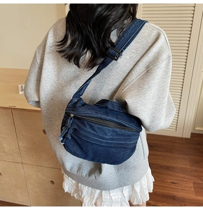 Detail of blue denim crossbody bag with adjustable strap worn over a grey sweatshirt