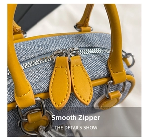 Detailed view of the smooth dual metal zippers on a denim shoulder bag with yellow leather trim