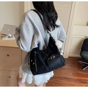 Detail of black pleated tote bag with silver buckle and white plush pendant accessory