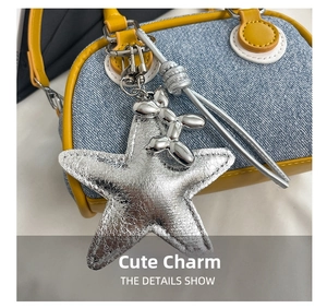 Detail of silver star charm and balloon dog pendant on denim and yellow leather bag