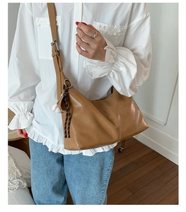 Detail of caramel crossbody bag with baseball charm and adjustable strap on a model