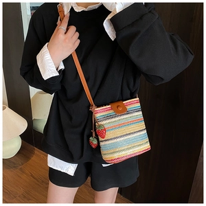 Detail of colorful hand-woven crossbody bag featuring cute strawberry charms and brown flap