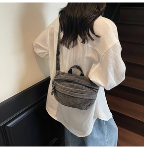 Rear view of a distressed charcoal denim crossbody bag with adjustable wide strap