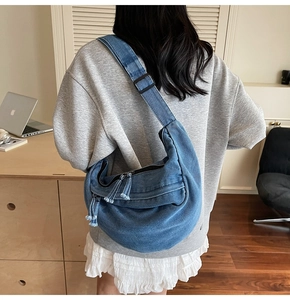 Detailed close-up of a blue denim crescent crossbody bag with zipper and tassel detail
