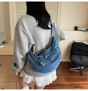 Detail of a large denim crescent moon bag with dual zippers and stylish tassels