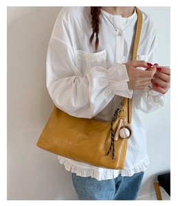 Close-up of ginger yellow hobo shoulder bag featuring a creative baseball charm pendant