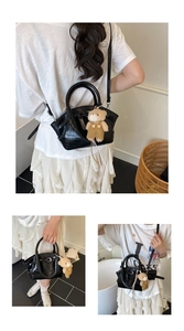 Detail view of black crocodile pattern handbag with cute teddy bear charm decoration