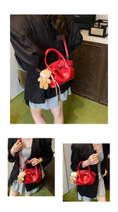 Detail view of red crocodile pattern handbag with bear charm and crossbody strap