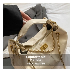 Detail showing the cream quilted texture, gold twist lock, and chain strap on the bag