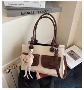 Detail of a two-tone tote bag with brown leather pockets and a cute plush bear charm