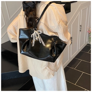 Détail du sac à bandoulière noir brillant avec nœud en dentelle et breloque perle