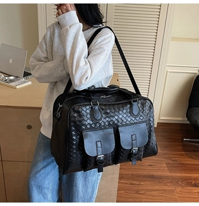 Detail of black woven leather travel bag featuring dual front pockets and adjustable strap