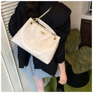 Detailed view of beige quilted tote bag featuring gold metal turn-lock and chain strap