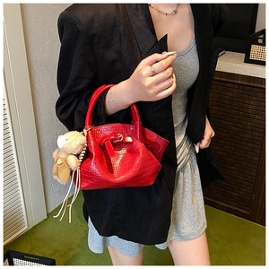 Detail of red crocodile pattern handbag with ribbon buckle and cute bear plush charm