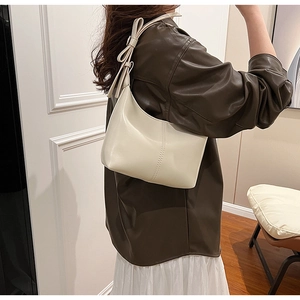 Détail d'un sac demi-lune blanc crème avec un nœud élégant sur la bandoulière réglable