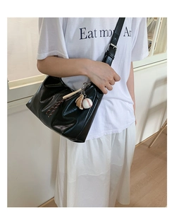 Détail d'un sac demi-lune en cuir noir avec breloque baseball et bandoulière réglable