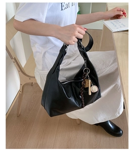 Detail of black leather croissant bag with silver zipper and baseball charm accessory