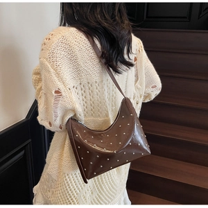 Detail of glossy caramel leather crossbody bag with silver studs on a shoulder strap
