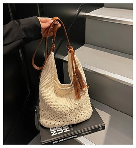 Primer plano de un bolso tipo cubo tejido en crema con borlas marrones y flores