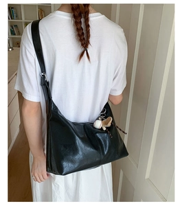 Détail d'un grand sac bandoulière noir avec un pendentif de baseball et gant de sport