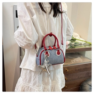 Close-up of gray denim shoulder bag with red leather trim and silver starfish charm