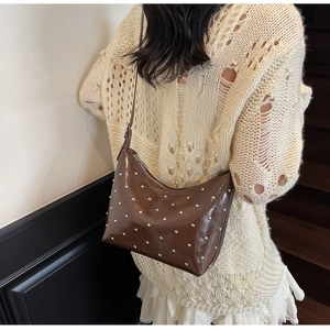 Detail of dark brown glossy patent leather bag with silver rivets in a crescent shape