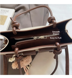 Detail of a smooth matte metal zipper and knotted handle on a brown patchwork handbag