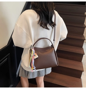 Détail du sac seau en cuir marron foncé avec un pompon arc-en-ciel coloré décoratif