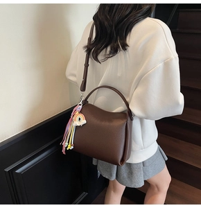 Détail du sac seau en cuir marron avec pompon coloré porté par un mannequin en intérieur
