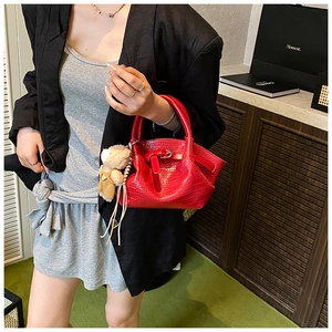 Detail of red crocodile texture bucket bag with bear pendant on model with black blazer