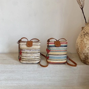 Rainbow woven straw bucket bags with strawberry charms on rustic stone steps