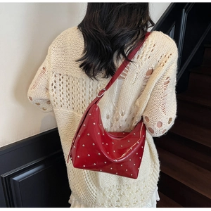 Close-up of red patent leather hobo bag with silver studs on a model's shoulder