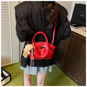 Detail of red crocodile texture bucket bag with adjustable strap and bear pendant