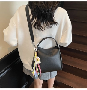Détail d'un sac seau en cuir grainé noir avec pendentif arc-en-ciel sur un escalier en bois