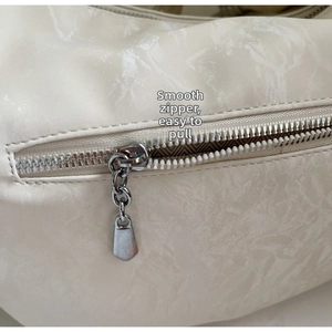 Detail of smooth metal zipper with decorative chain on cream large capacity shoulder bag