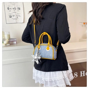 Detail of blue denim bowling bag with yellow leather trim and silver star pendant accessory