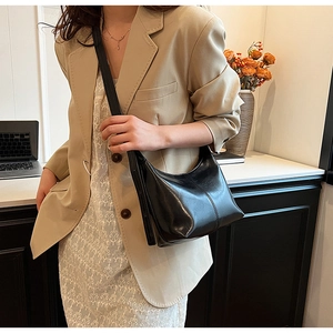 Gros plan d'un sac hobo en cuir noir brillant avec des coutures verticales sur le modèle