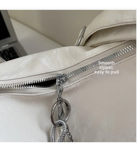 Close-up of a white tote bag featuring a smooth silver zipper and metallic chain detail